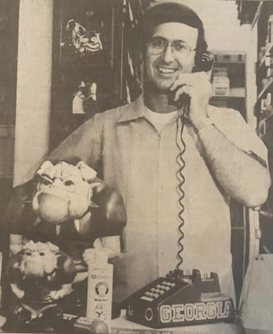 Jimmy Parker on the telephone behind the counter, surrounded by Georgia
                  Bulldogs souvenirs
